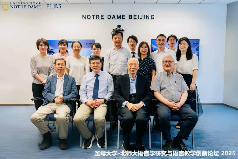 Group photo of twelve people seated and standing in front of a wall with the Notre Dame Beijing logo.
