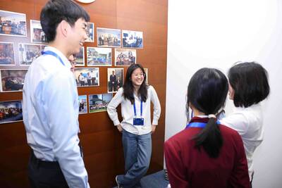 Students smile while interacting by a wooden wall with Notre Dame Global Gateway photos.