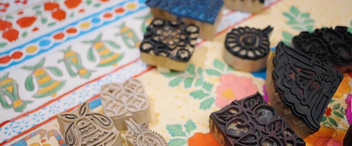 A collection of varied wooden and rubber block printing stamps on two distinct colorful fabrics with floral and bell designs.