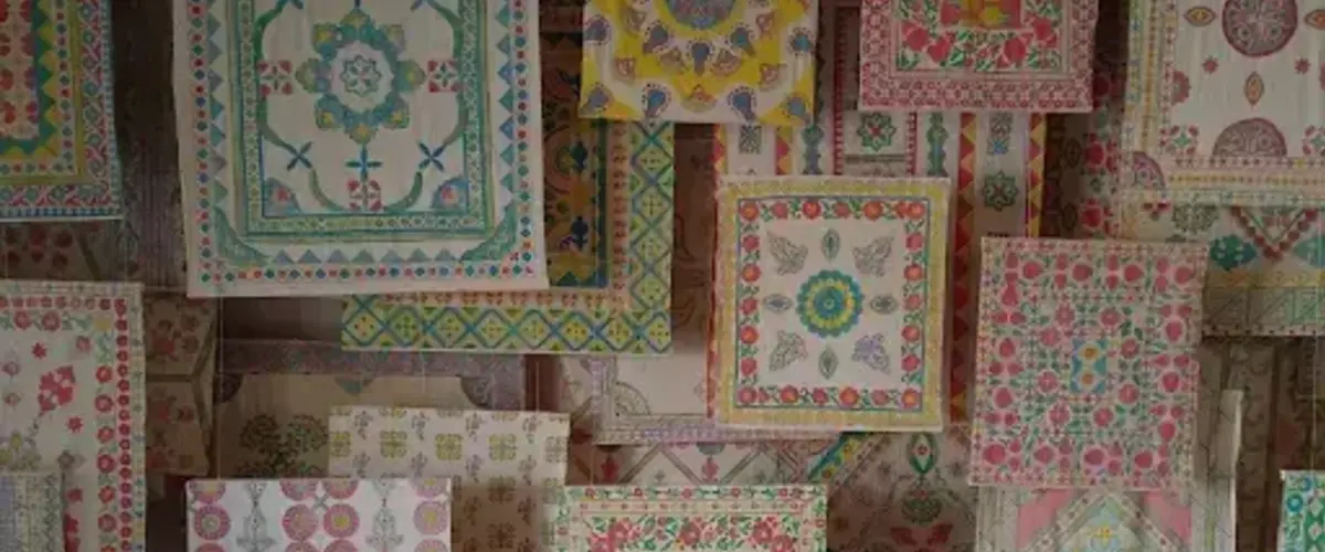 Colorful, patterned textiles hang vertically, featuring intricate floral and geometric designs in teal, pink, yellow, and green.